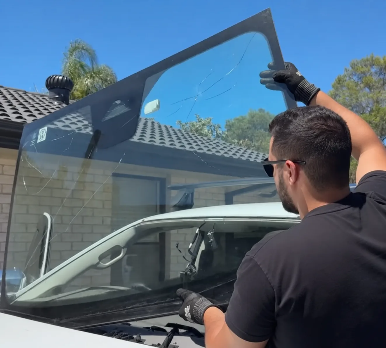 A technician lifting a windscreen into position outside a house.
