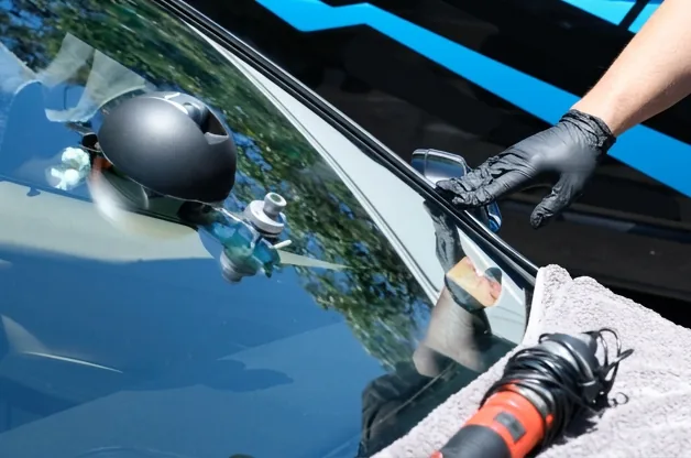 A technician working on a windscreen at the kerbside, with hand tools laid out on a towel across the bonnet.