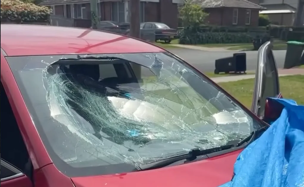 A car with a badly smashed windscreen parked in a suburban street, waiting for a replacement.