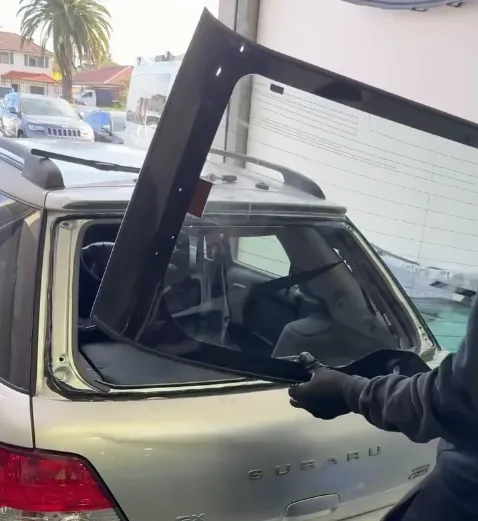 Rear glass being lifted out of a station wagon tailgate at the kerbside.
