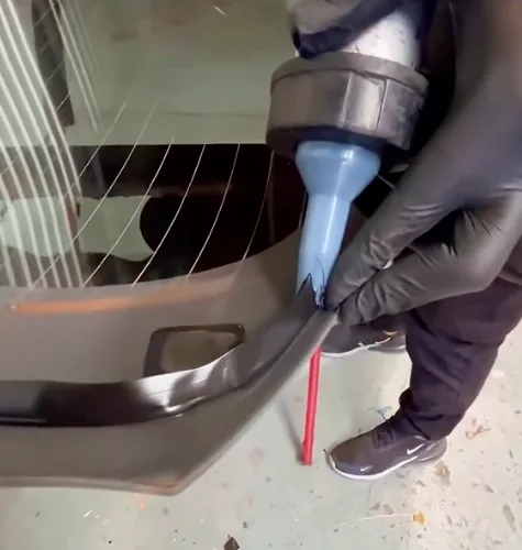 A gloved hand running primer along the edge of a rear glass panel, with demister lines visible behind it.