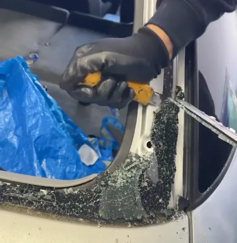 Old adhesive being cut back from a tailgate aperture, with broken glass still gripped around the frame.