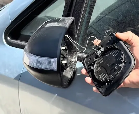 A mirror backing plate held away from its housing, with the heating element wires still connected between the two.