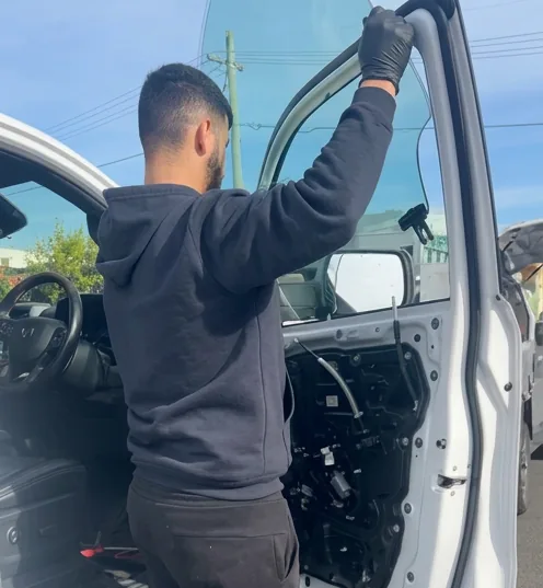 A technician working at the open door of a white van with the interior door trim removed.