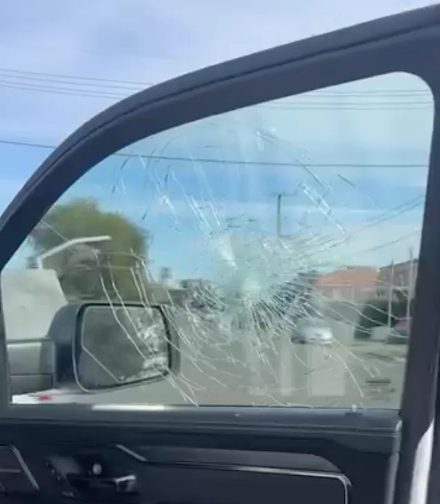A shattered driver's door window on a van, the glass crazed across its full width but still held in the frame.