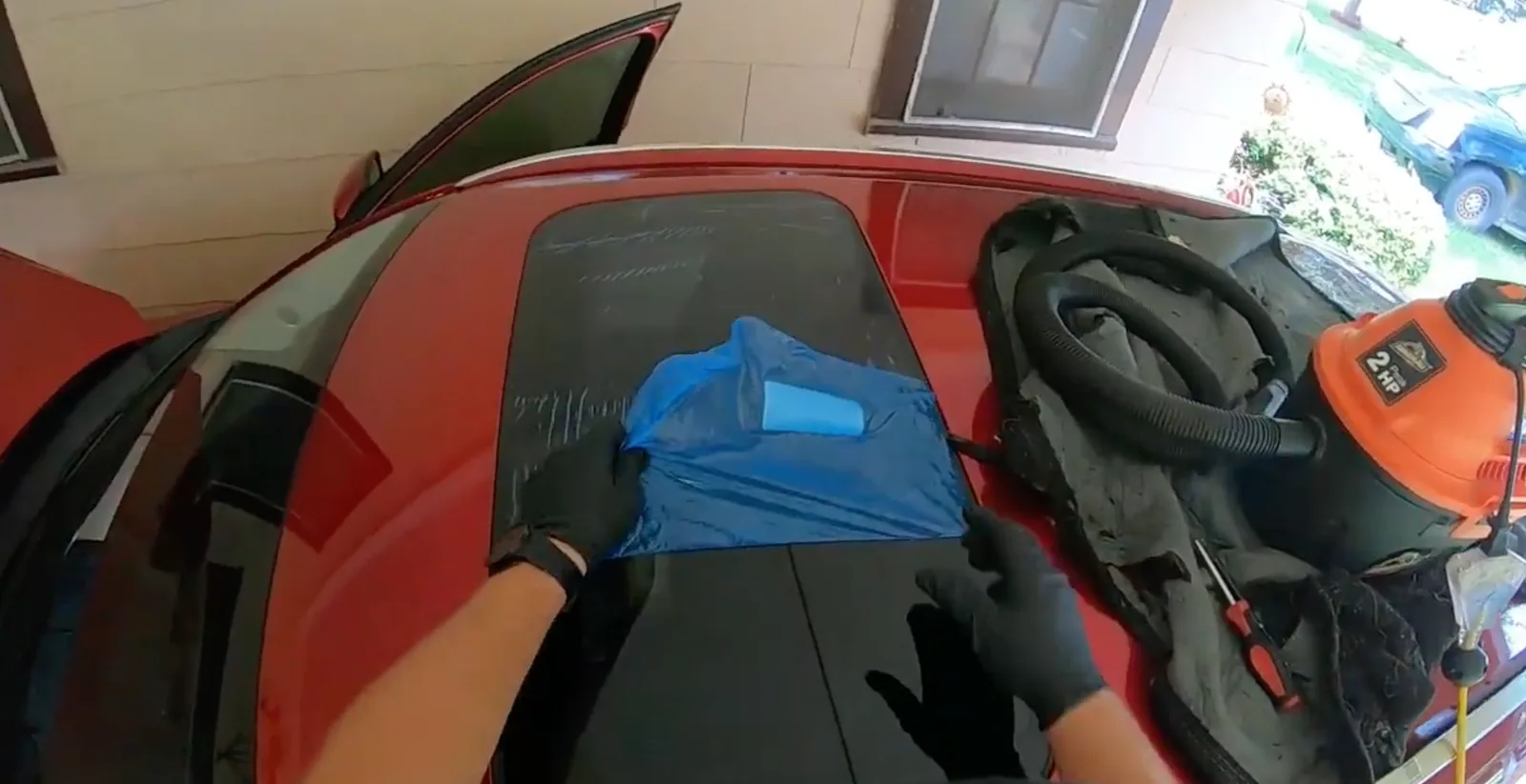 A technician working on the roof glass of a red car parked in a driveway.