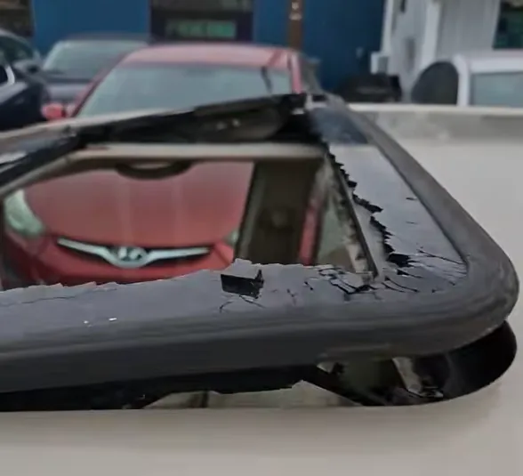 A removed sunroof frame with shattered glass still gripped around its edge, resting beside the vehicle.