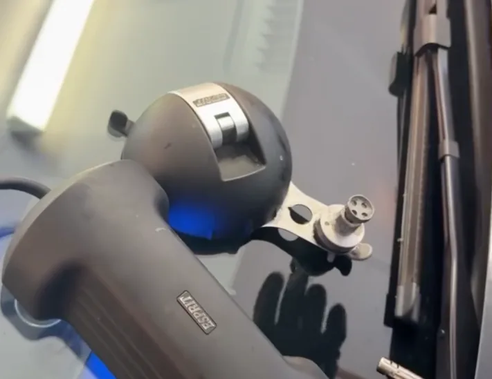 A resin injector clamped to a windscreen above the wiper cowl, part way through a chip repair.