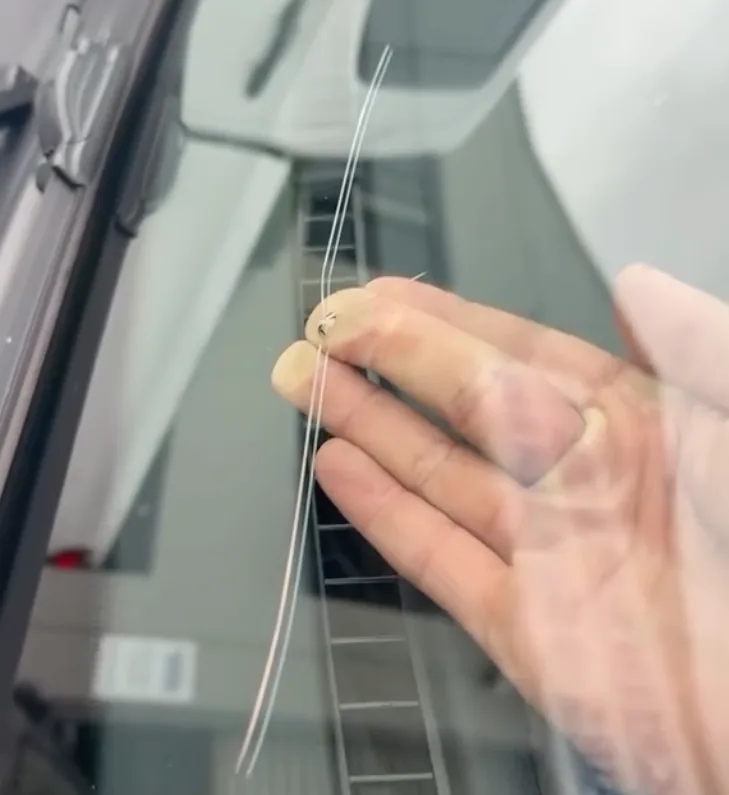 A technician's hand following the line of a long crack running across a windscreen.