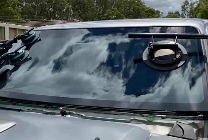 A windscreen held on suction cups against the frame of a four wheel drive, ready to be lifted out.