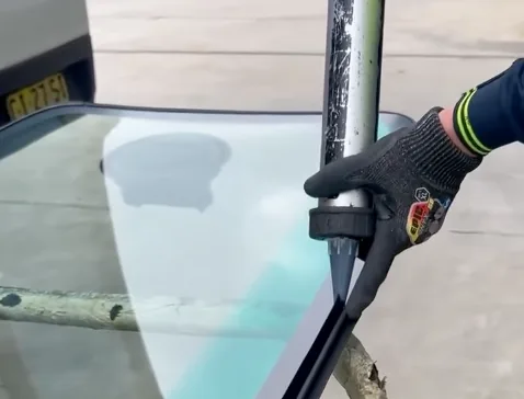 A gloved technician running a bead of urethane adhesive along the edge of a windscreen with a cartridge gun.