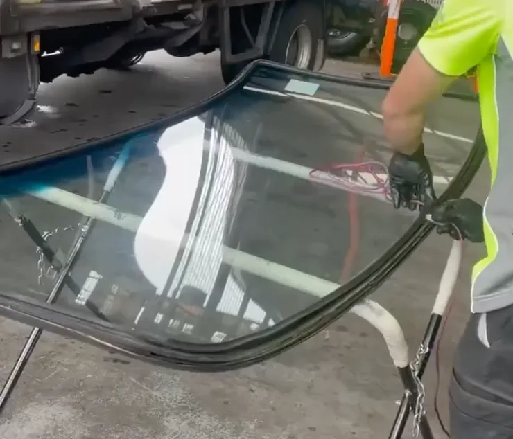 A technician in a high visibility shirt lifting a windscreen clear of a vehicle in a carpark.