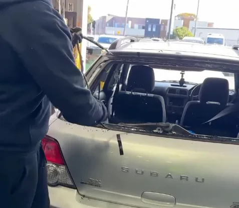 A technician cutting bonded glass out of a station wagon tailgate at the kerbside.
